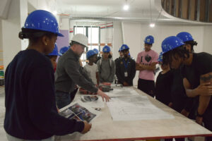 A group of people in hard hats looking at blueprints in a construction space.